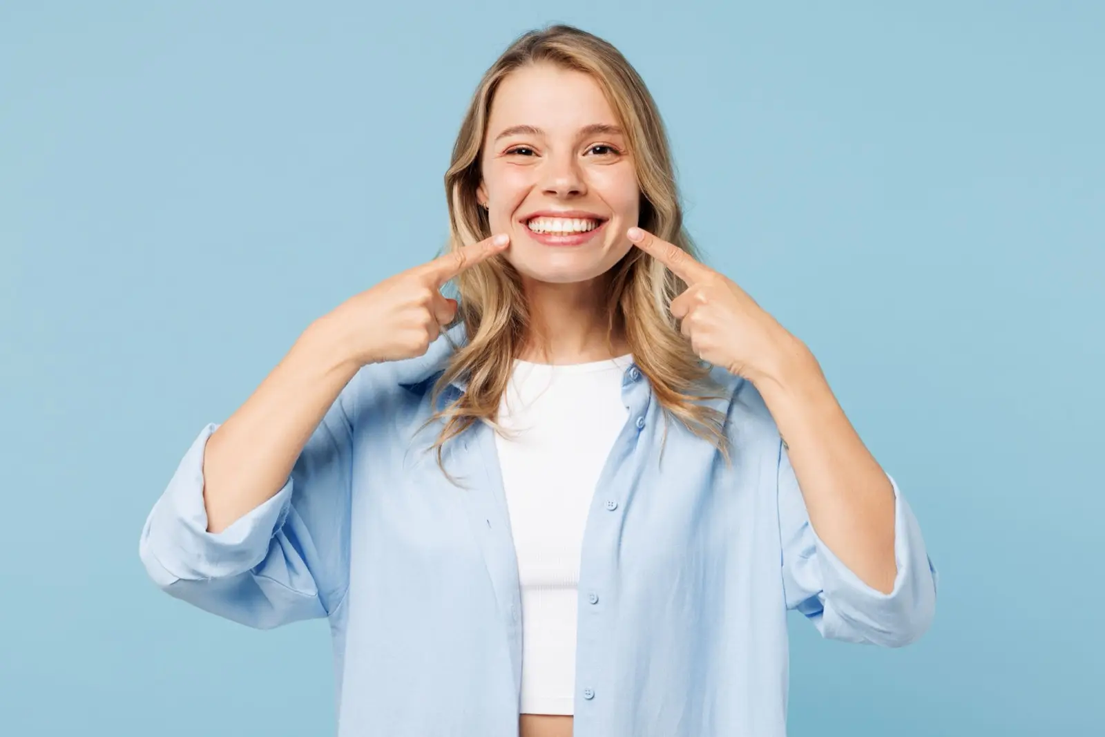 a woman is pointing at her teeth and smiling .