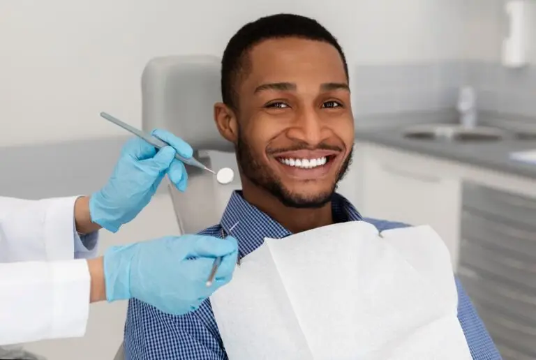 Smiling man in a dental chair with a dentist's gloved hands holding tools.